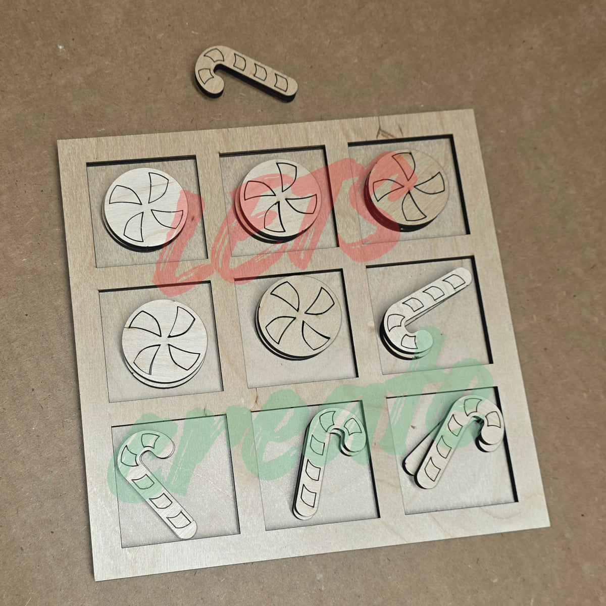 A laser-cut wooden Tic-Tac-Toe board featuring layered candy cane and peppermint candy game pieces resting neatly inside the board's slots.